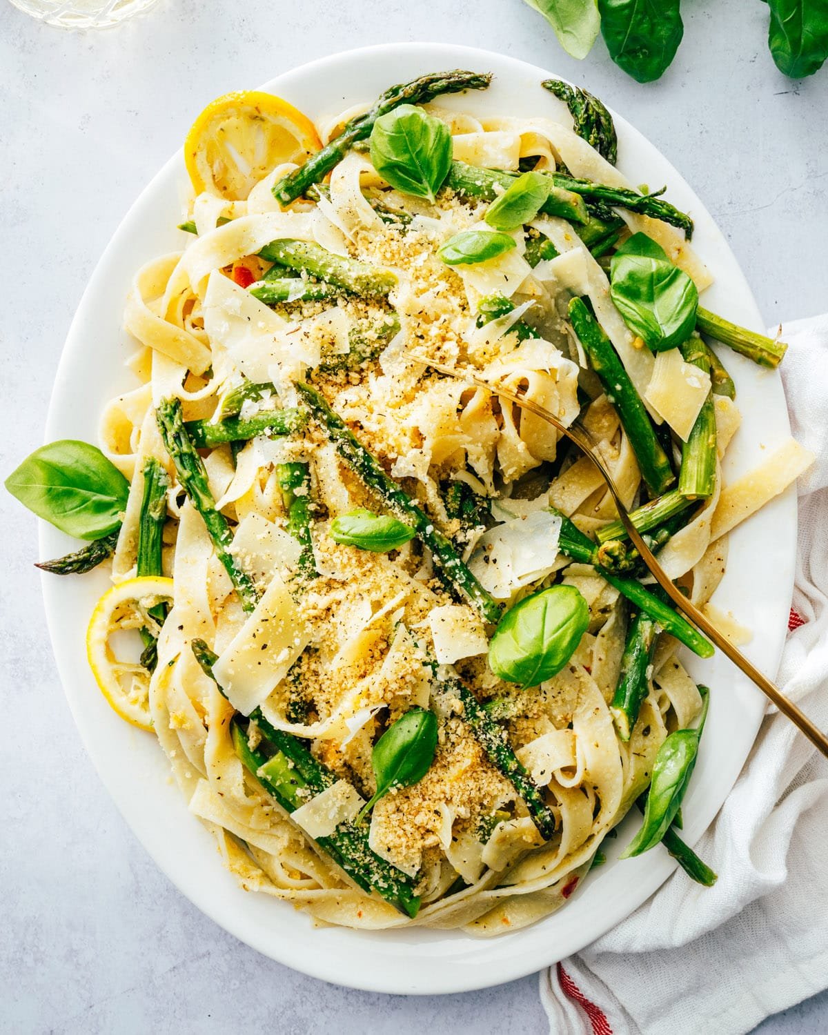 Spring recipes: asparagus pasta on a serving platter with basil leaves and lemon garnish.