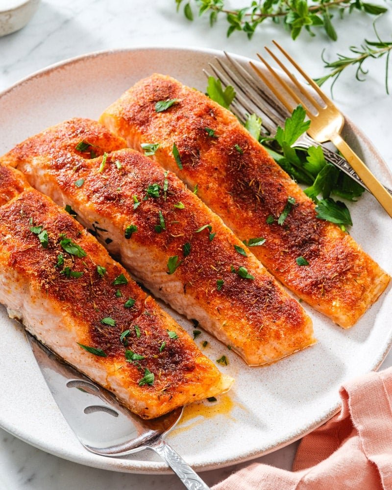 Oven baked salmon on a plate with serving forks and garnished with parsley.