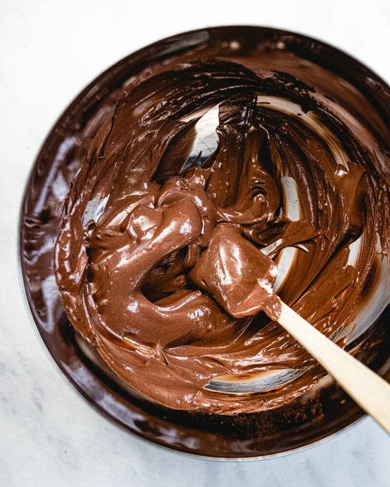 A small glass bowl with chocolate pudding being scraped from the sides with a cooking utensil