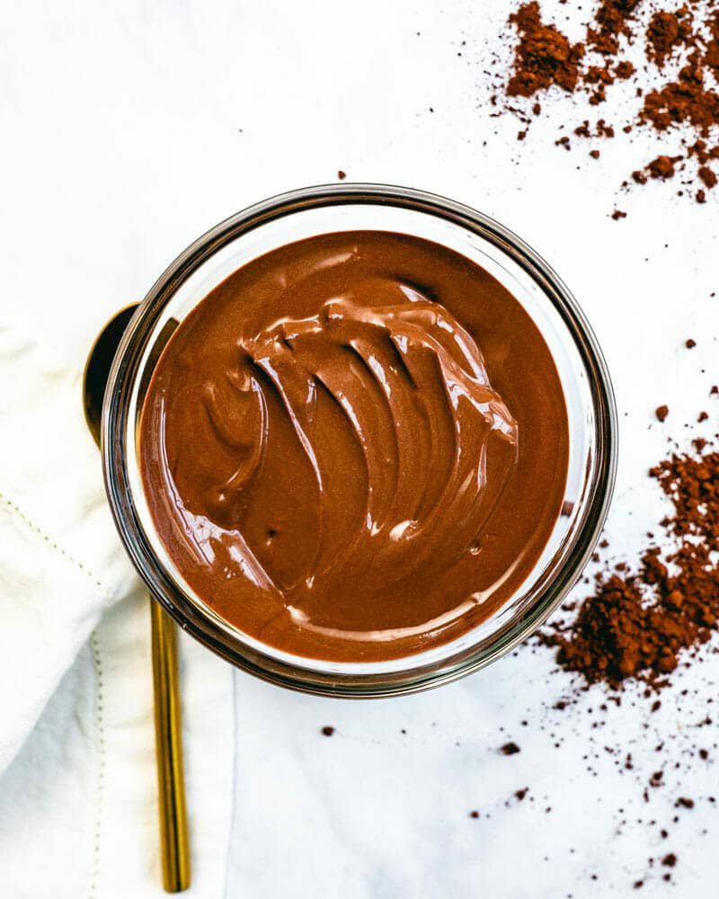 Creamy chocolate pudding in a bowl, surrounded by a golden spoon and dark cocoa powder