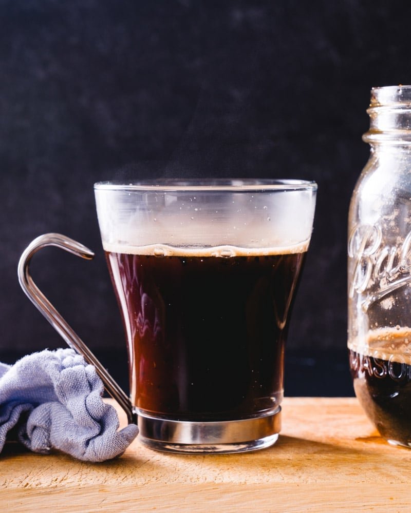 a cup of coffee in a glass cup with an interesting hook handle