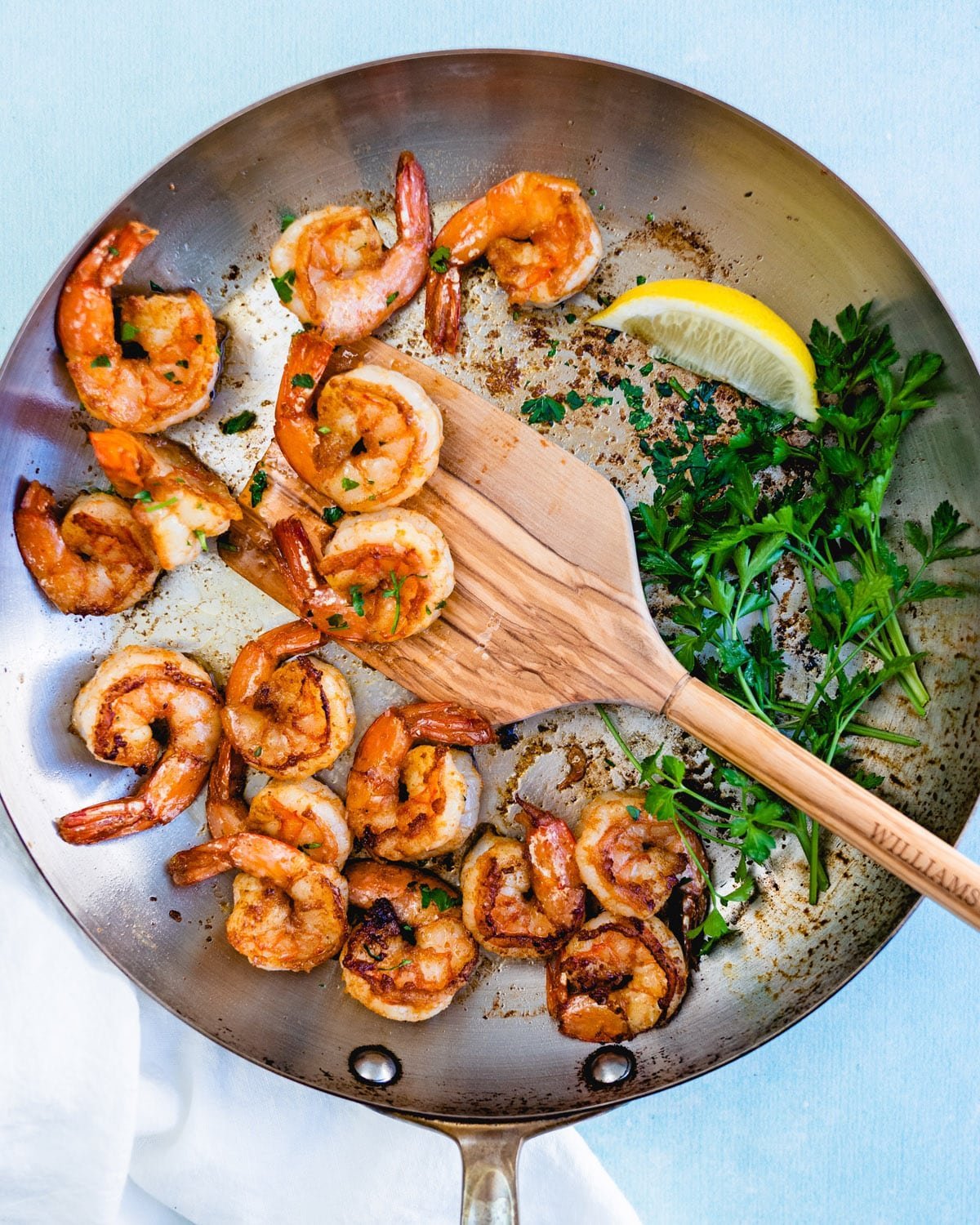 Overhead view of shrimp being served from a a frying pan with green herbs and a lemon on the side.
