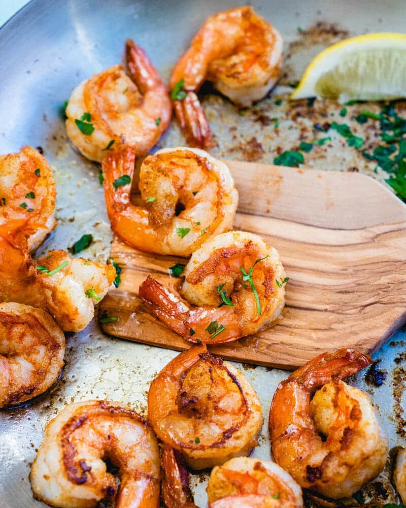 cooked shrimp being stored with a spatula with a lime wedge on the side in a frying pan